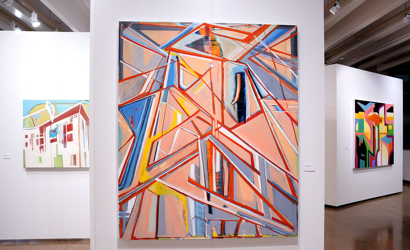 Three paintings hang in a gallery. The painting on the left features a house with square windows, the larger center painting is full of stripes and jagged lines and the far right is of more lines and curves.