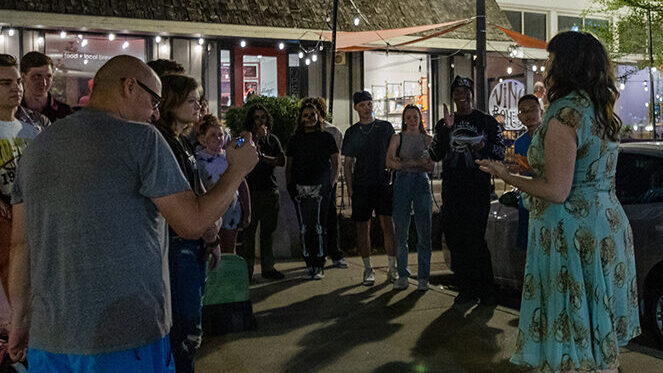 A theater instructor addresses a crowd gathered around her outside of a cafe.