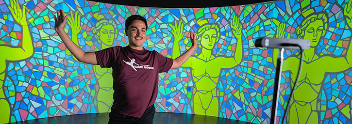 A college student dances in an immersive environment, with artificial intelligence technology used to display his movements on the screen behind him.