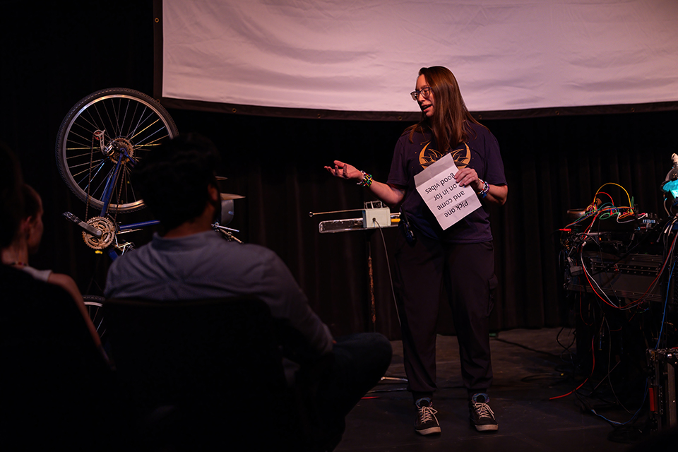 A college professor stands on a stage, discussing an event for the audience.
