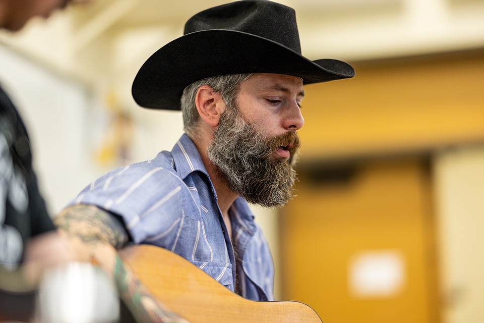 A country music performer sings and plays guitar in a classroom setting.