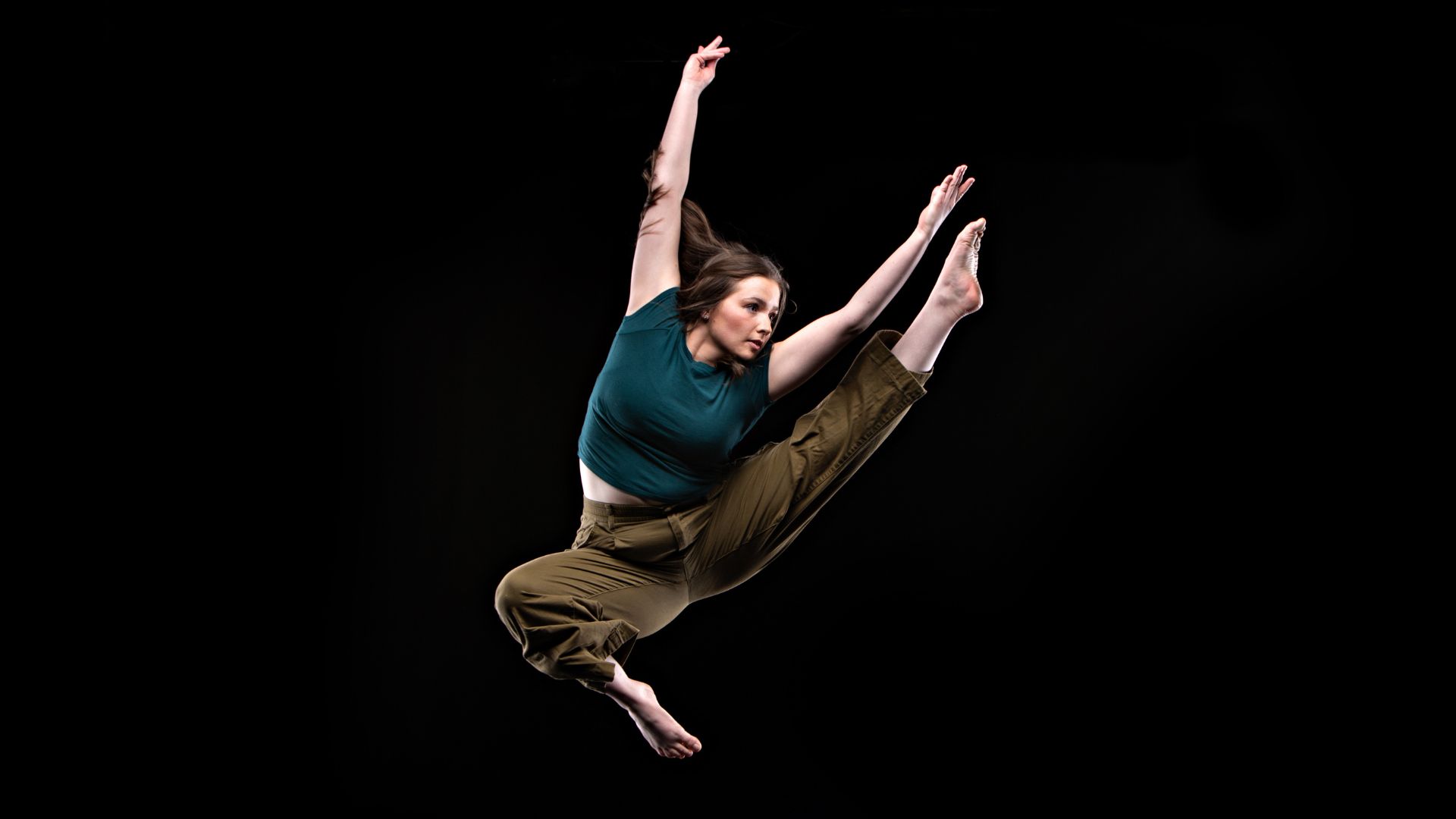 A dancer is shown in in midair, with her arms extended up, and her left leg extended out.