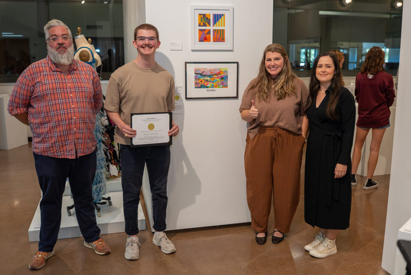 Four people stand in an art gallery and pose for a photo among art on the wall.