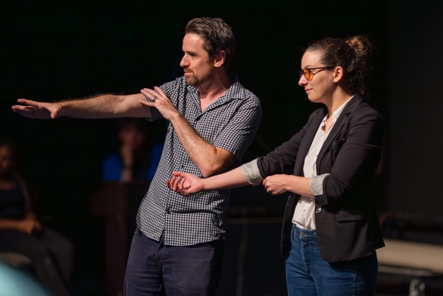 Two university professors stand in a black box theatre.