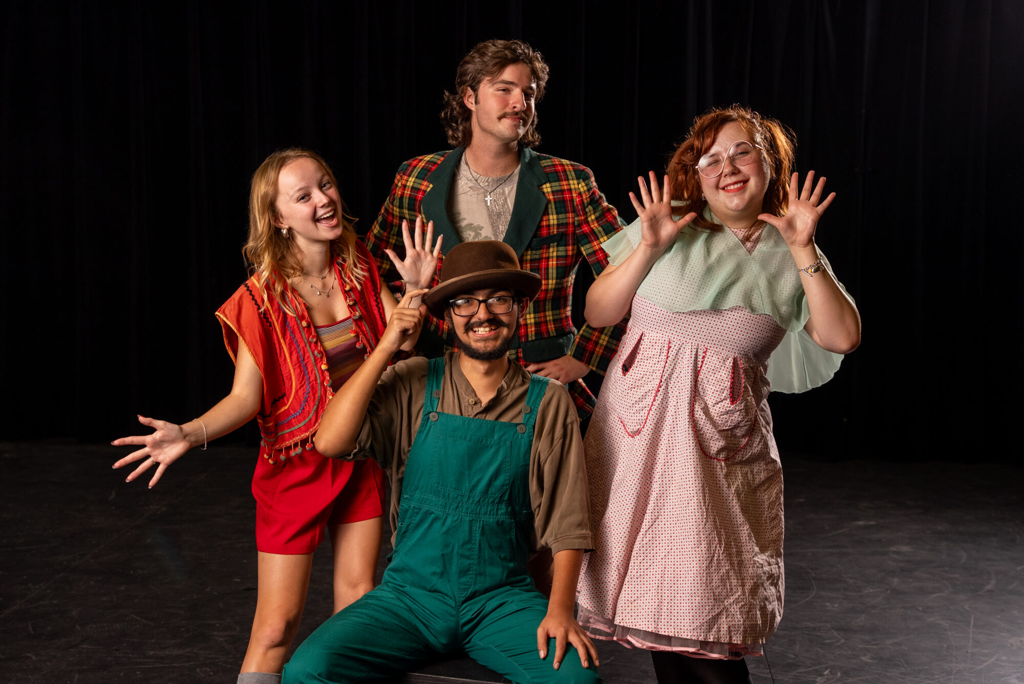 Four theatre students stand and pose for a photograph. they are dressed in costumes for a play they are in.