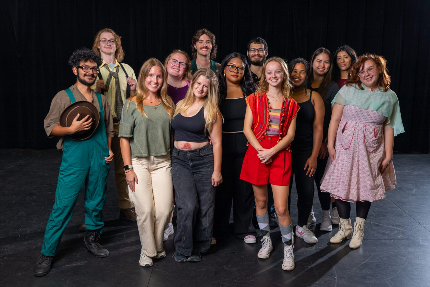 Thirteen university students pose for a photograph in a black box theatre.