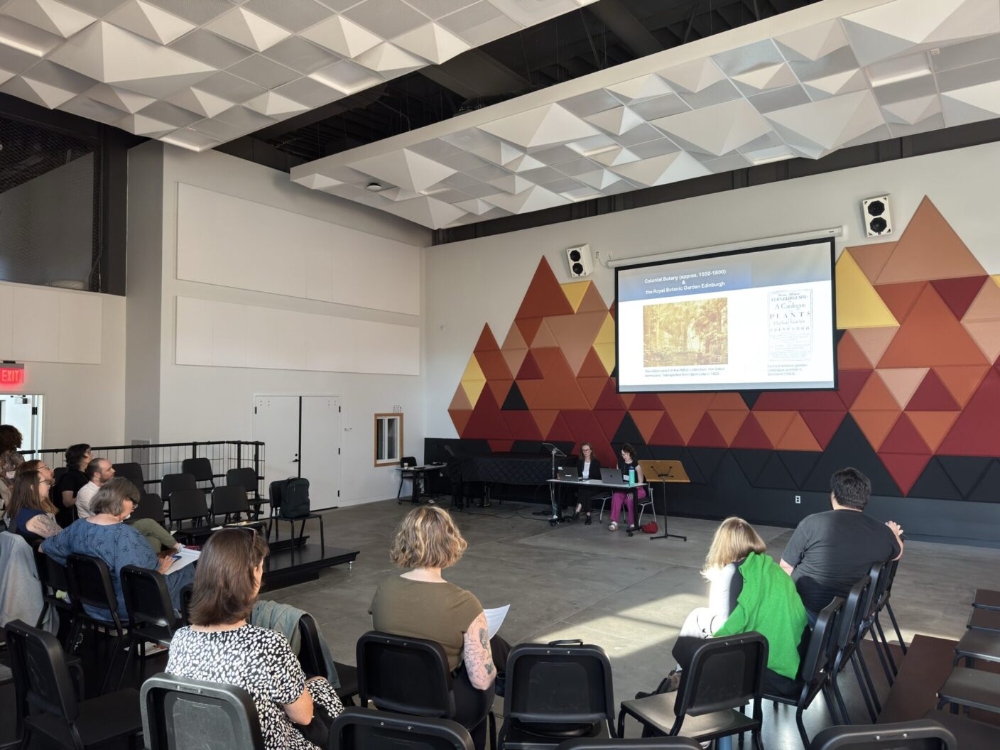 University professors present powerpoint slides in a classroom of people sitting in chairs.