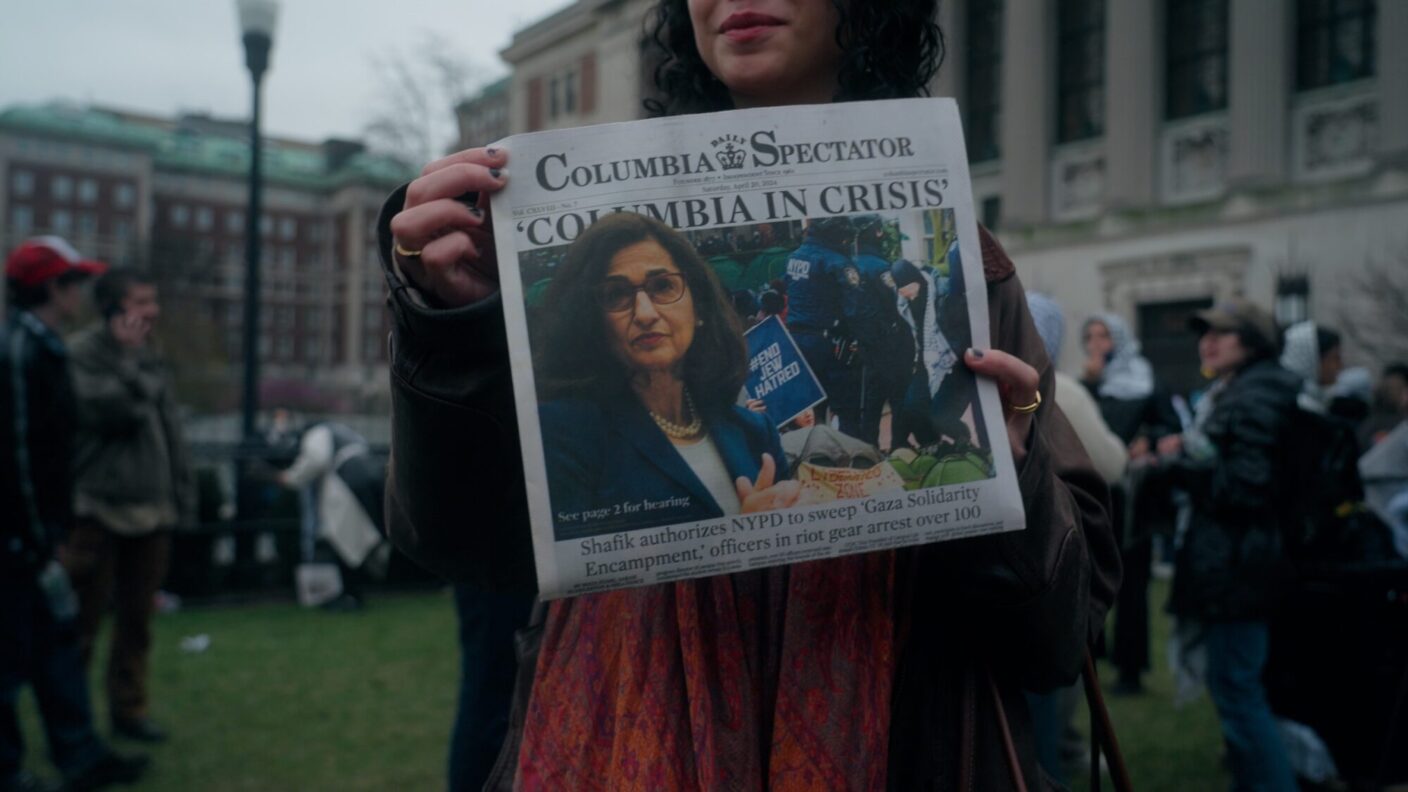 A college student holds up the Columbia Spectator newspaper with the headline "COLUMBIA IN CRISIS."