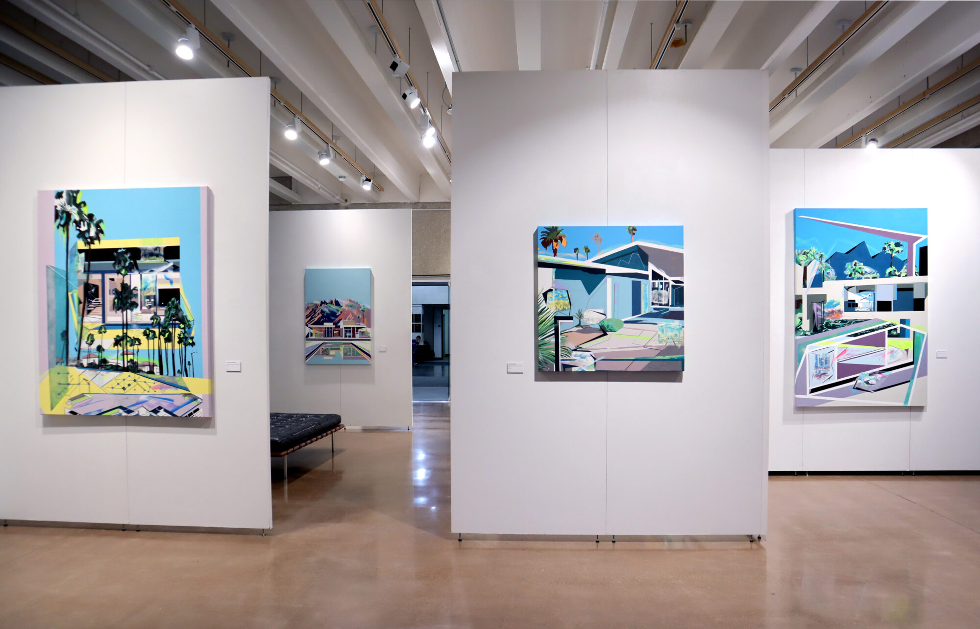 Four landscape paintings of houses and palm trees hang in a university art gallery.