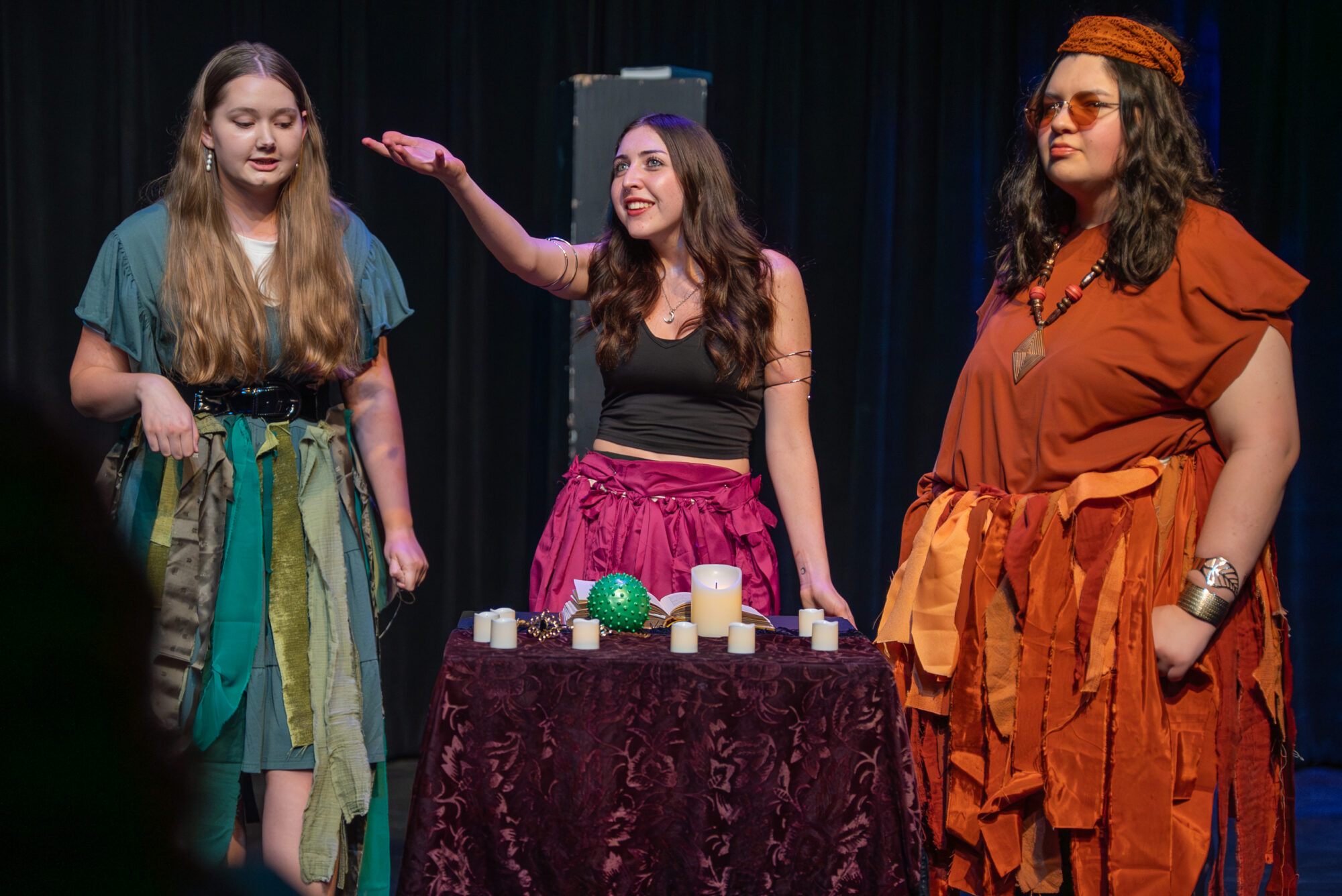 Three university students perform in a play in a black box on a university campus. Each student is in a retro 70s outfit.