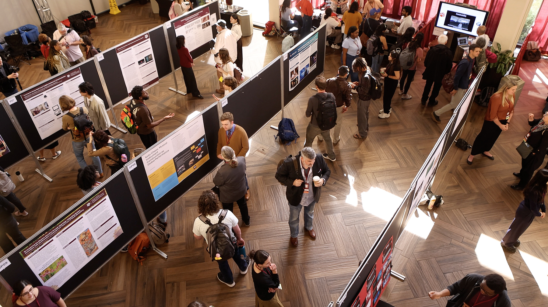 Students and faculty surround dozens of poster boards on display in an auditorium on a university campus.